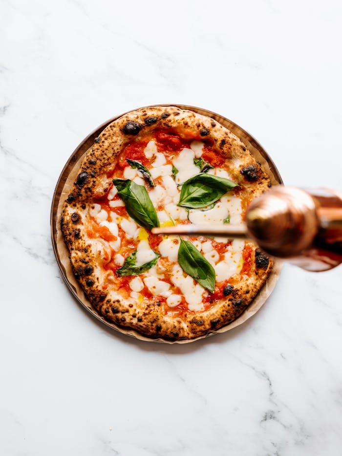 Top view of a margherita pizza on marble, garnished with fresh basil leaves.